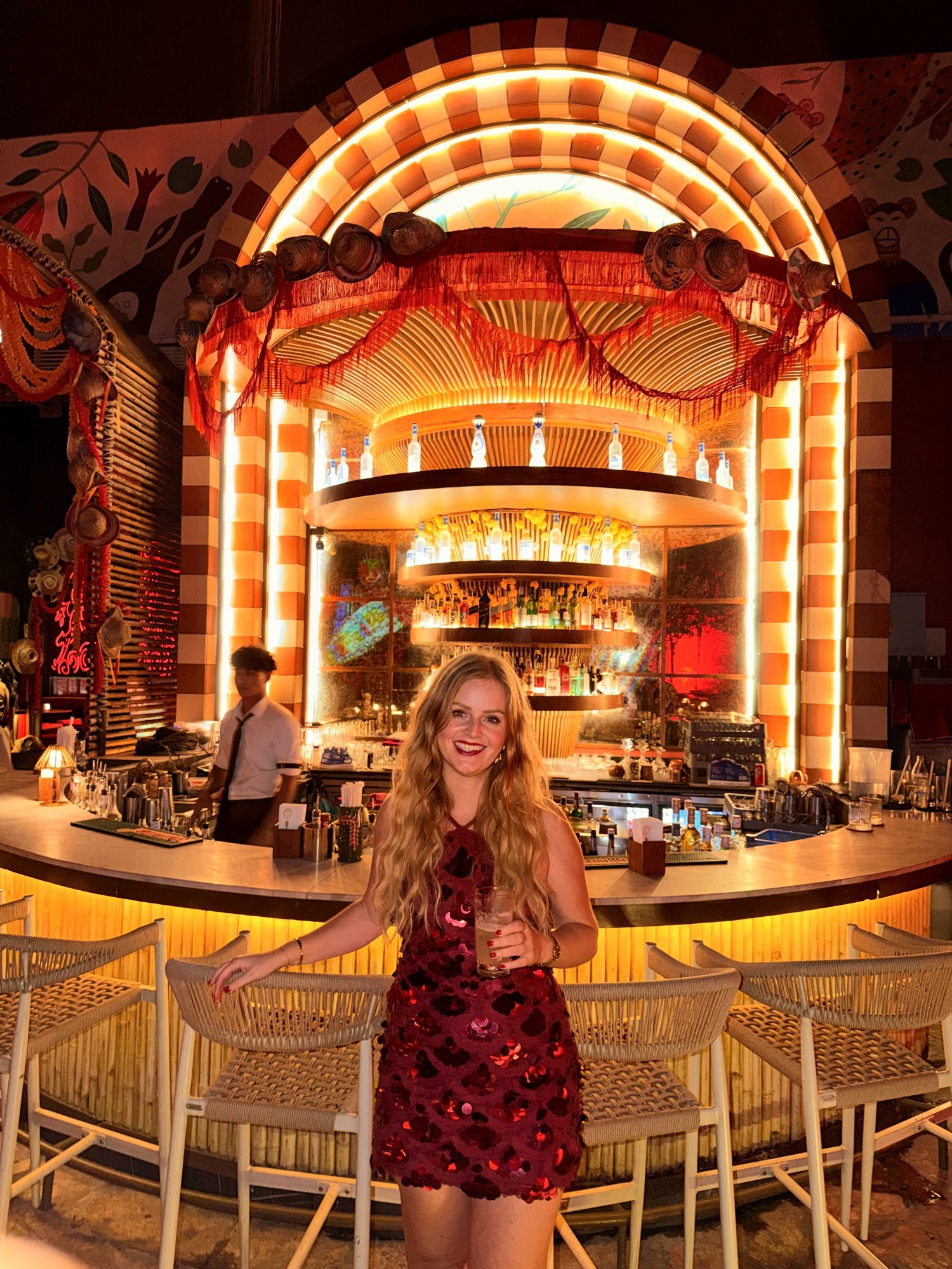 Jeanella in a red dress in front of an illuminated orange bar